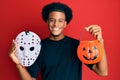 African american man with afro hair wearing hockey mask and halloween pumpking smiling with a happy and cool smile on face