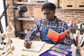 African american man artist drawing on notebook reading book at art studio Royalty Free Stock Photo