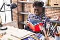African american man artist drawing on notebook reading book at art studio Royalty Free Stock Photo