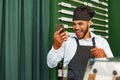 African american man barista using his smartphone and laughing while standing at the counter of coffee shop Royalty Free Stock Photo
