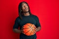 African american man with braids holding basketball ball smiling looking to the side and staring away thinking Royalty Free Stock Photo