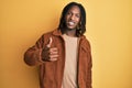 African american man with braids wearing brown retro jacket doing happy thumbs up gesture with hand