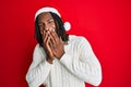 African american man with braids wearing christmas hat laughing and embarrassed giggle covering mouth with hands, gossip and