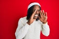 African american man with braids wearing christmas hat shouting angry out loud with hands over mouth Royalty Free Stock Photo