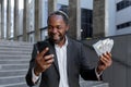 African american man in business suit rejoices, got online small business loan, owner with money cash dollars happy with Royalty Free Stock Photo