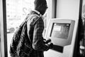 African american man in checkered shirt with backpack holding wallet in hand against atm. Black man traveler