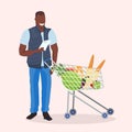 African american man checking shopping list happy male customer with trolley cart buying products in grocery market