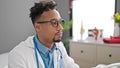 African american man doctor sitting on table with relaxed expression at clinic Royalty Free Stock Photo