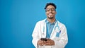 African american man doctor smiling using smartphone over isolated blue background Royalty Free Stock Photo