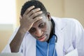 African American man doctor unhappy boring hand touching head using laptop and holding paperwork checking report at table office