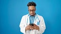 African american man doctor using smartphone over isolated blue background Royalty Free Stock Photo