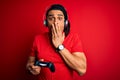 African american man with dreadlocks playing video game using joystick and headphones cover mouth with hand shocked with shame for Royalty Free Stock Photo