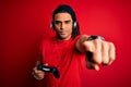African american man with dreadlocks playing video game using joystick and headphones pointing with finger to the camera and to Royalty Free Stock Photo