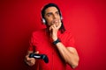 African american man with dreadlocks playing video game using joystick and headphones serious face thinking about question, very Royalty Free Stock Photo