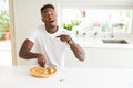 African american man eating cheese pizza at home with surprise face pointing finger to himself Royalty Free Stock Photo