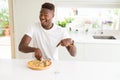 African american man eating cheese pizza at home very happy pointing with hand and finger Royalty Free Stock Photo