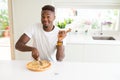 African american man eating cheese pizza at home very happy pointing with hand and finger to the side Royalty Free Stock Photo