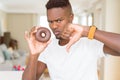 African american man eating chocolate donut with angry face, negative sign showing dislike with thumbs down, rejection concept