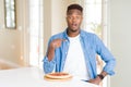 African american man eating pepperoni pizza at home with surprise face pointing finger to himself Royalty Free Stock Photo