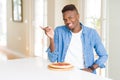 African american man eating pepperoni pizza at home very happy pointing with hand and finger to the side Royalty Free Stock Photo