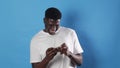 an African-American man gambles in a smartphone while standing on a blue background.