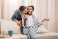 african american man gifting ring in heart shaped box to woman sitting on couch Royalty Free Stock Photo