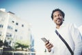 African American man in headphones standidng in sunny street listening to songs on smart phone, checking e-mail using Royalty Free Stock Photo