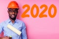 African American man with helmet hardhat white on pink wall with roller brush tool drawing new year 2020 paint orange