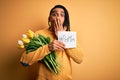 African american man holding best mom message paper and tulips celebrating mothers day cover mouth with hand shocked with shame