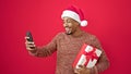 African american man holding christmas gift having video call over isolated red background