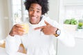 African American man holding and drinking glass of orange juice very happy pointing with hand and finger Royalty Free Stock Photo