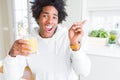 African American man holding and drinking glass of orange juice very happy pointing with hand and finger to the side Royalty Free Stock Photo
