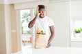 African american man holding paper bag full of fresh groceries with happy face smiling doing ok sign with hand on eye looking Royalty Free Stock Photo