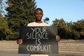 African American man holding sign with phrase Your Silence Is Complicit outdoors. Racism concept