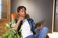 African American man holding tablet, sitting in chair, looking thoughtful in a modern business offic Royalty Free Stock Photo