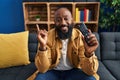 African american man holding television remote control smiling happy pointing with hand and finger to the side Royalty Free Stock Photo