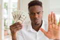 African american man holding twenty dollars bank notes with open hand doing stop sign with serious and confident expression, Royalty Free Stock Photo