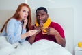 African american man in knitted scarf and redhaired ginger woman in pajamas lying in bed day off from work because they Royalty Free Stock Photo