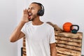 African american man listening to music using headphones at the gym shouting and screaming loud to side with hand on mouth Royalty Free Stock Photo