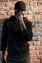 African american bandit man in mask standing by brick wall, hooligan in black wear