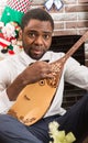 African American man with Musical instrument Dombra by fireplace. Christmas