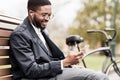 African-american man with phone sitting on bench near bicycle Royalty Free Stock Photo