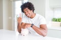 African American man putting a coin inside piggy bank happy with big smile doing ok sign, thumb up with fingers, excellent sign Royalty Free Stock Photo