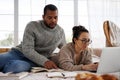 African american man reading book and talking to asian girlfriend in eyeglasses using laptop on bed at home Royalty Free Stock Photo