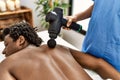 African american man reciving back massage with gun percusion at beauty center Royalty Free Stock Photo