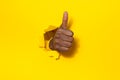 African american man showing thumbs up, doing approval gesture through hole in ripped yellow paper, copy space Royalty Free Stock Photo