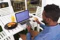 African american man sitting in cafe using laptop and smartphone drinking coffee eating breakfast Royalty Free Stock Photo