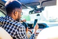 african american man sitting in a car and adjusting rearview mirror looking to phone map app