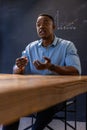 African american man sitting at classroom table explaining line graph on chalkboard Royalty Free Stock Photo