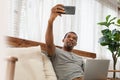 African American man sitting on couch doing online video chat on smartphone Royalty Free Stock Photo